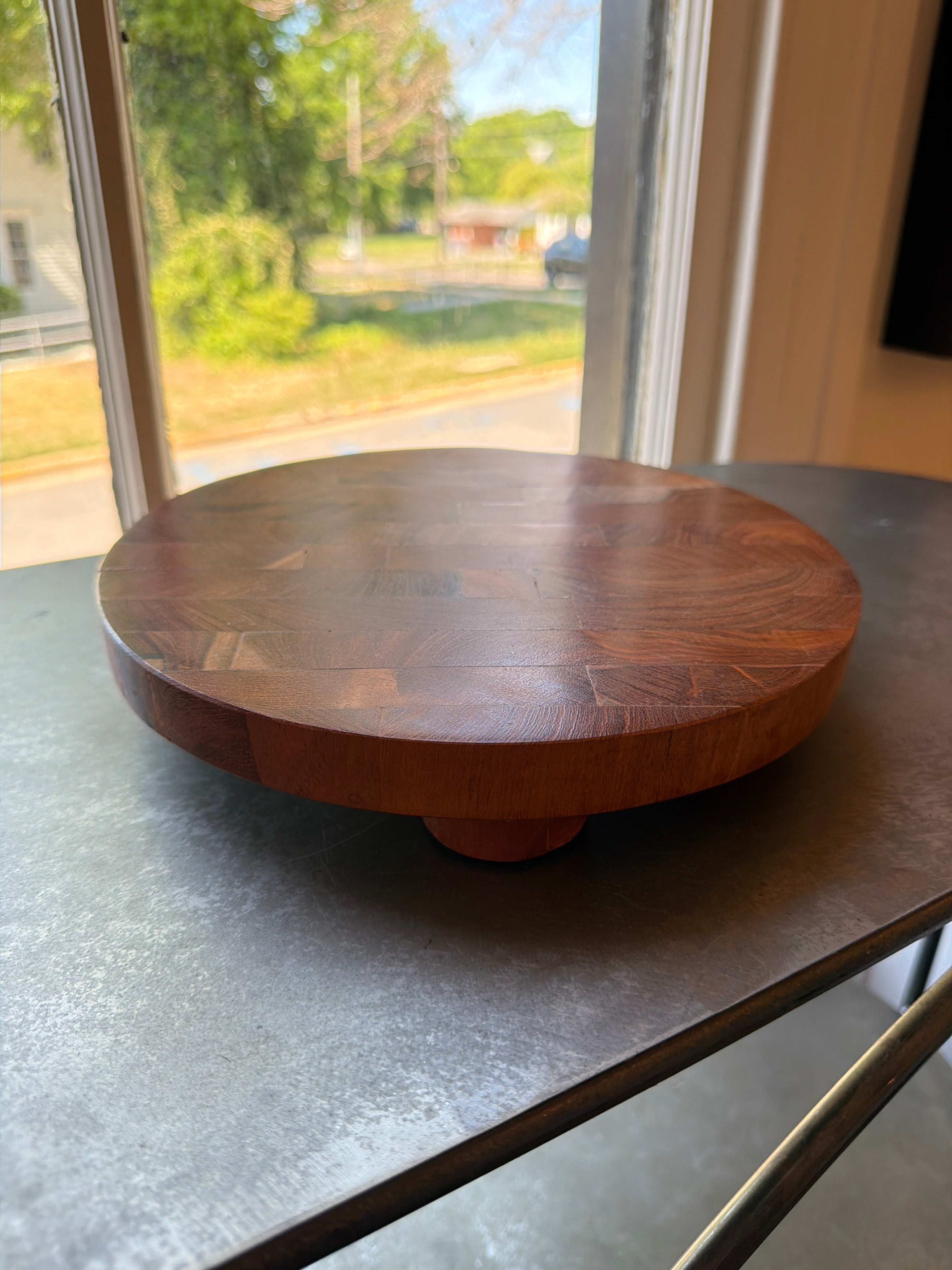 Wood Cake Stand, Small with rich wood grain pattern sits on a metal table by a sunlit window, perfect for kitchen decor, gifts, and entertaining from Knotty and Board.