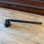 Flame On Main Candle Snuffer with a sleek black metal handle and bell-shaped cover resting on a wooden surface, perfect for safe candle extinguishing in home decor. 1