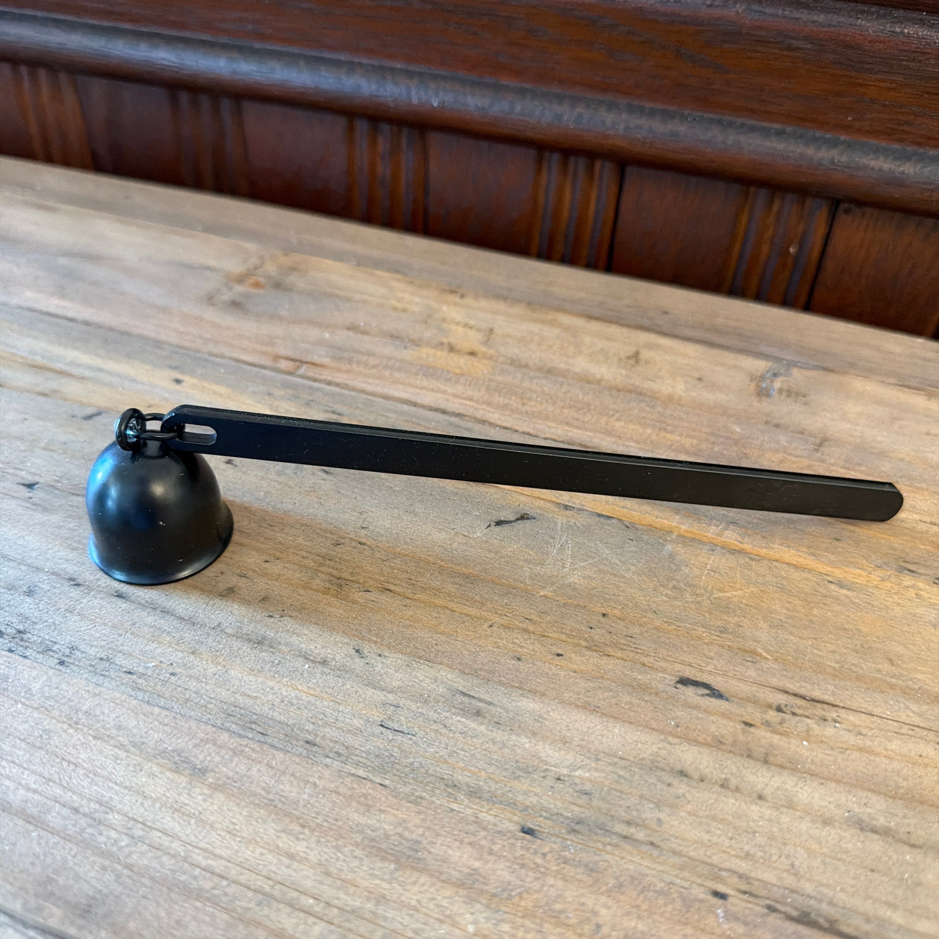 Flame On Main Candle Snuffer with a sleek black metal handle and bell-shaped cover resting on a wooden surface, perfect for safe candle extinguishing in home decor.