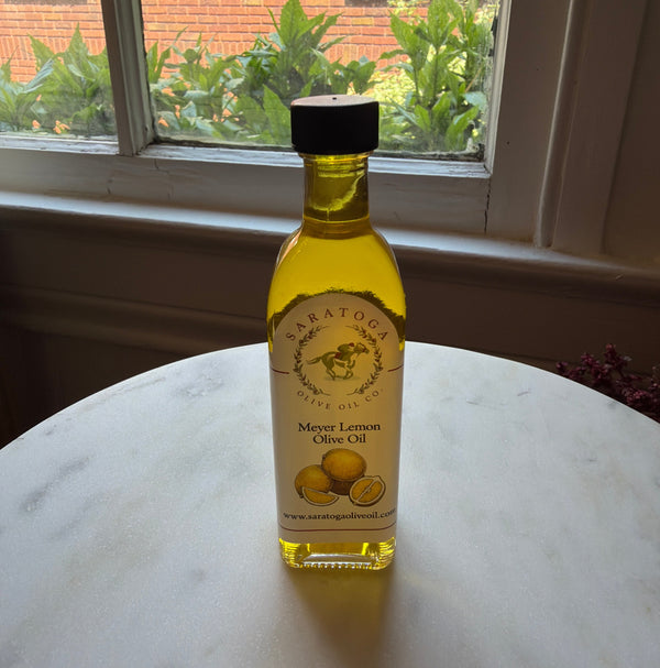 Bottle of Saratoga Olive Oil, 60 ml, Meyer Lemon Oil on a marble table in a cozy kitchen setting with natural light from the window in the background.