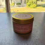 Rockaway Travel Candle 4oz French Citrus in a gold tin with pink label sitting on a windowsill with sunlight and outdoor greenery in the background, curated decor and gifts from Knotty and Board. 1
