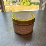Rockaway Travel Candle 4oz Sunday Morning in a small tin with yellow lid, placed on a table near a sunlit window, perfect for home decor or gifts from Knotty and Board. 1