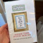 Hand holding a Deluxe Cross Stitch Kit, Here the Fuck We Go, featuring a framed subversive cross stitch pattern with floral accents, perfect for funny home decor or gifts from Knotty and Board, promoting humor and style in any room. 1