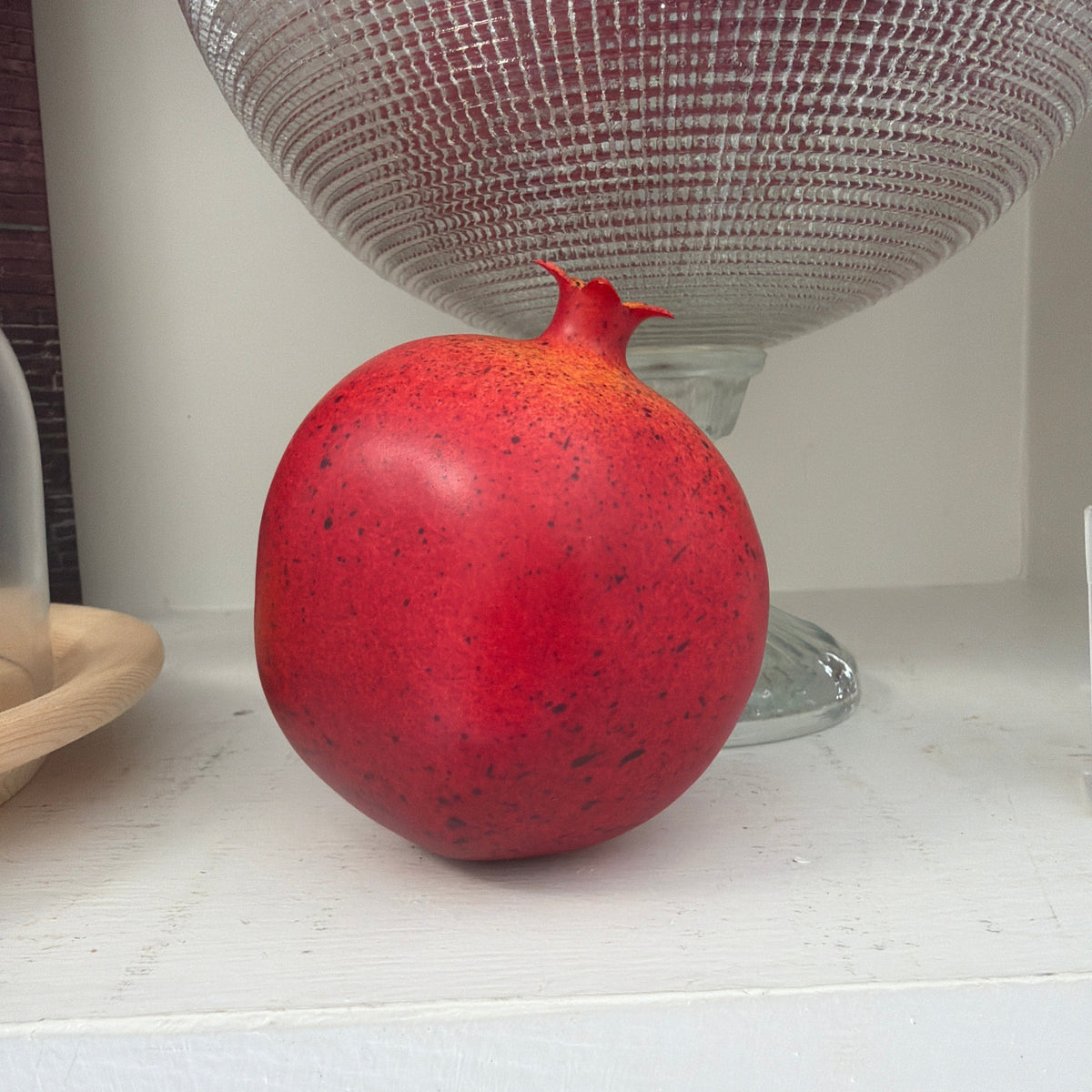 Pomegranate - Display sitting on a white shelf next to decorative glassware, perfect for adding a pop of color and unique decor to kitchen or dining spaces at Knotty and Board.