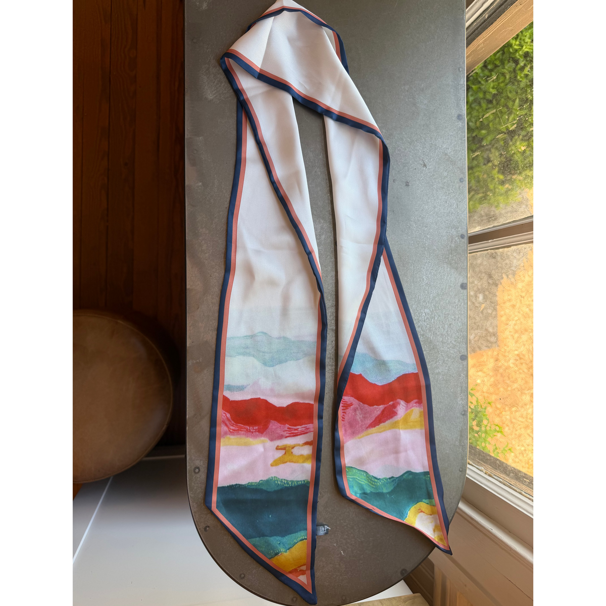 Agate Scarf, Multi-color with abstract watercolor design in tones of red, pink, green, and yellow, displayed on a rustic tabletop near a window, perfect for stylish decor or gifts from Knotty and Board.