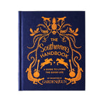Hardcover book titled The Southerner's Handbook: A Guide to Living the Good Life with orange decorative illustrations on a navy blue cover, offered by Knotty and Board, an independent retail for decor and gifts. 1
