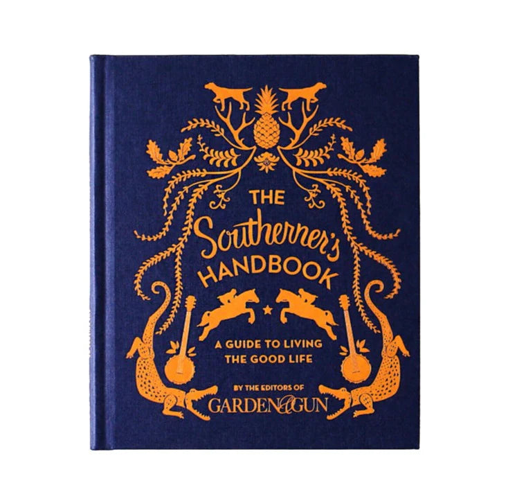 Hardcover book titled The Southerner's Handbook: A Guide to Living the Good Life with orange decorative illustrations on a navy blue cover, offered by Knotty and Board, an independent retail for decor and gifts.