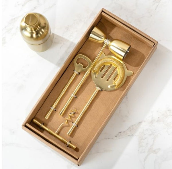 Gold Stick Bar Set 4 PC. displayed in a box on a marble surface, featuring a cocktail shaker, bottle opener, corkscrew, jigger, and strainer in polished gold finish, perfect for stylish entertaining.