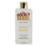 A clear glass bottle filled with colorful wooden matches with multi-colored tips and a gold cap, labeled 