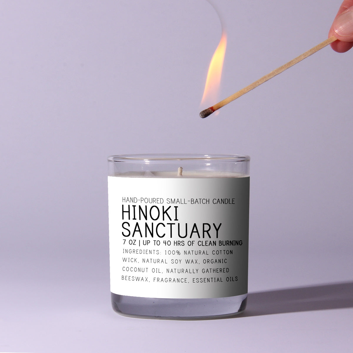 Just Bee Hinoki Sanctuary Candle, 7 oz. with a lit match above it, ready to ignite, showcasing a hand-poured, natural soy wax candle ideal for decor and gifting from Knotty and Board.