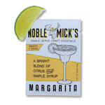 Packet of Noble Mick's Single Serve Craft Cocktail, Margarita flavor, featuring bright citrus and simple syrup blend, accompanied by a fresh lime wedge, promoting Knotty and Board gifts and decor. 1
