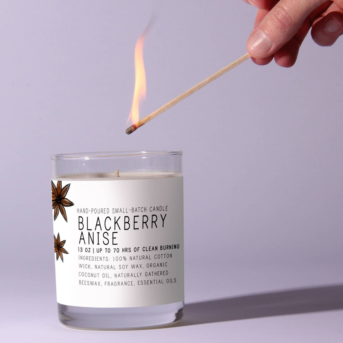Hand lighting a Just Bee Blackberry Anise, 7 oz candle with natural ingredients and clean-burning wick, ideal for cozy home decor and thoughtful gifts from Knotty and Board.