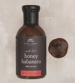 Bottle of Finch & Fennel Sweet Heat Honey Habanero BBQ Sauce, 13.5 oz with a small pool of sauce beside it, perfect for kitchen gifts from Knotty and Board, independent retail with curated decor. 1