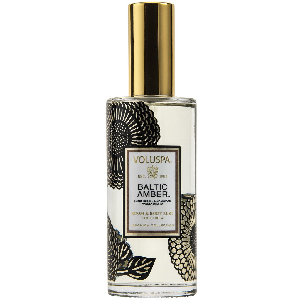 Voluspa Baltic Amber Room & Body Spray in a clear glass bottle with black floral designs and a shiny gold cap, perfect for adding elegant decor and fresh scents.