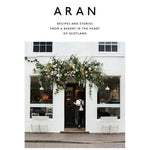 Cover of Aran: Recipes and Stories from a Bakery in the Heart of Scotland - Flora Shedden featuring a charming bakery entrance adorned with lush floral decor, reflecting Knotty and Board’s curated gifts and kitchen ambiance. 1