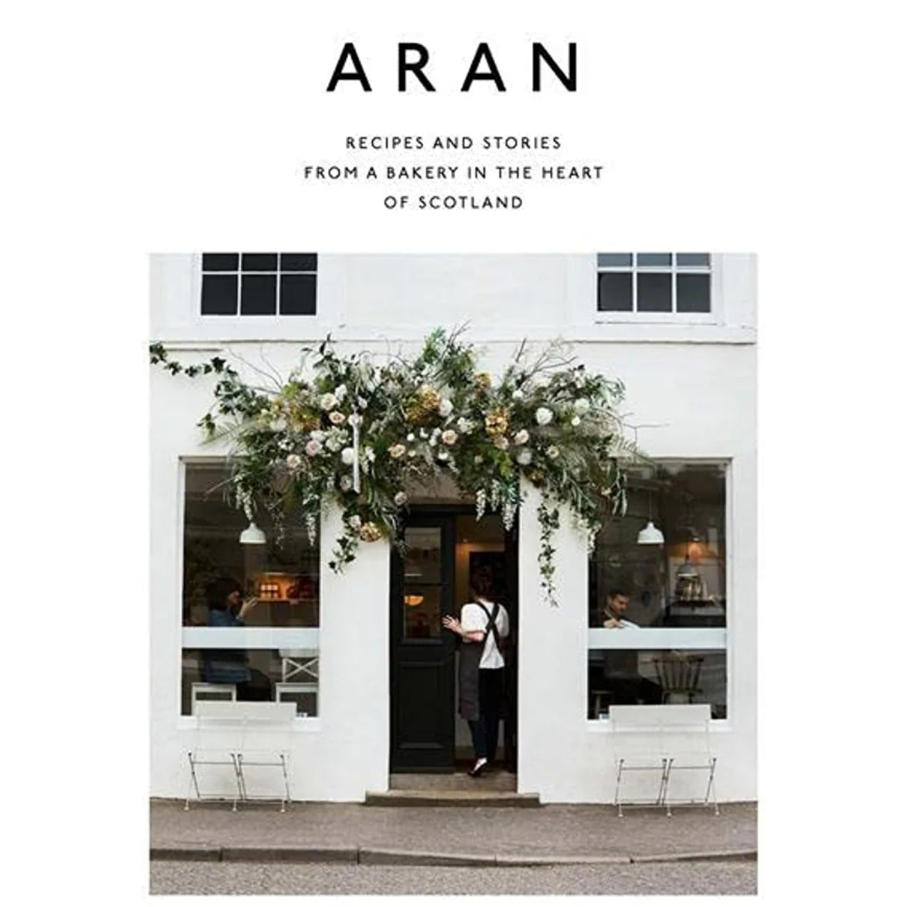 Cover of Aran: Recipes and Stories from a Bakery in the Heart of Scotland - Flora Shedden featuring a charming bakery entrance adorned with lush floral decor, reflecting Knotty and Board’s curated gifts and kitchen ambiance.