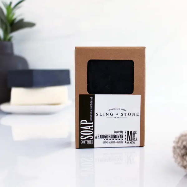 Men's Soap, Hardworking Man, Plum Amber Citrus, 5 oz. in eco-friendly brown packaging with black and white label, displayed on a clean surface with blurred decor in the background.