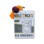 Noble Mick's Single Serve Craft Cocktail, Old Fashioned box next to a cherry and orange peel garnish, styled for entertaining and gift decor by Knotty and Board. 1