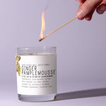 Hand lighting a Just Bee Ginger Pamplemousse, 13 oz candle in a glass jar with a clean, modern label, perfect for decor and gifts from Knotty and Board. 1