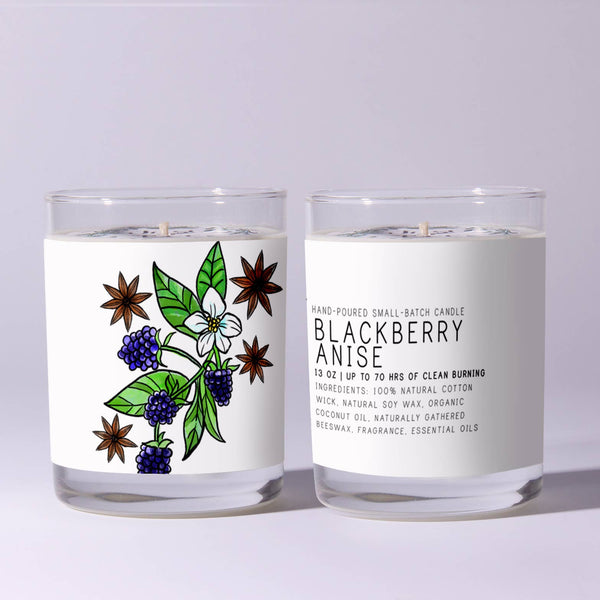 Two clear glass candles with white wax, one showing a colorful botanical illustration of blackberries, anise stars, and green leaves, the other displaying product text for Just Bee Blackberry Anise, 7 oz, on a light gray background.
