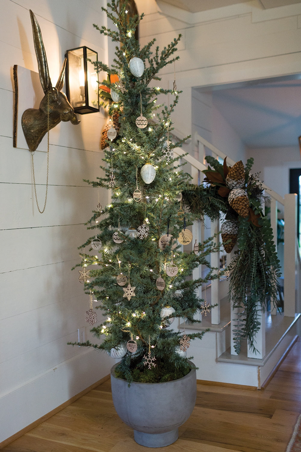 E&E Brass Wall Mount, Eric displayed in a cozy room next to a decorated lit Christmas tree in a modern planter by a staircase with festive greenery and pinecone accents, perfect for holiday decor and gifts from Knotty and Board.