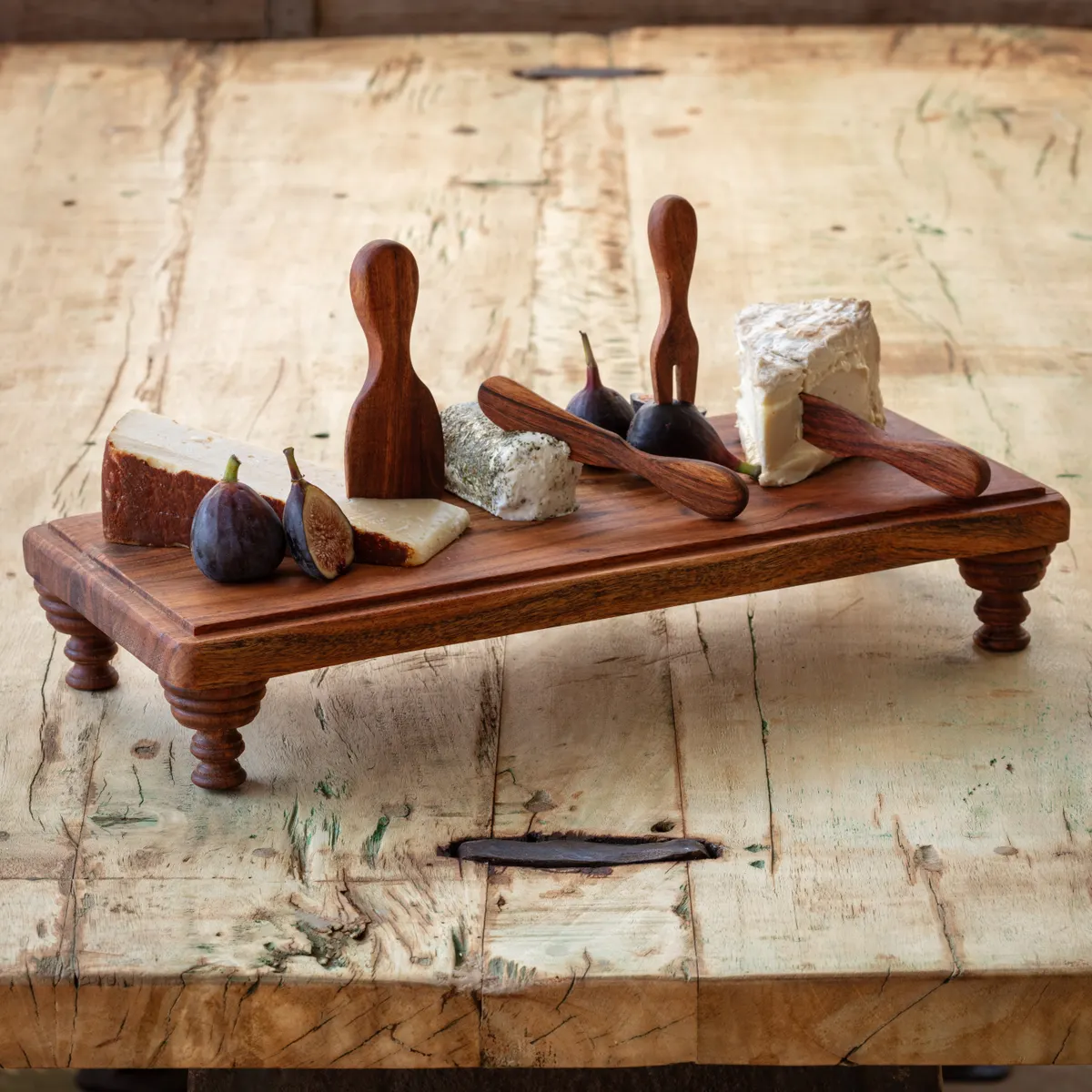 Wooden Serving Riser 18 X 8 X 3 displaying an assortment of cheeses and fresh figs with wooden spreaders on a rustic wooden table, ideal for kitchen and dining decor.