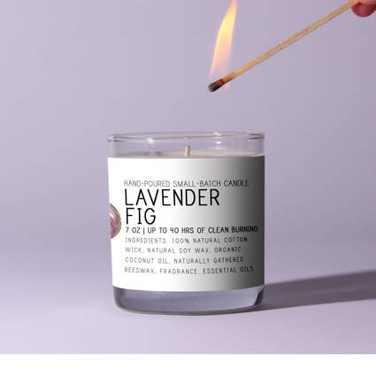 Just Bee Lavender Fig Candle - 7 oz in a clear glass jar with minimalist label, shown being lit with a match, perfect for cozy decor and gifts from Knotty and Board.