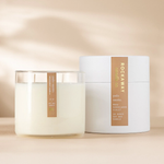 Rockaway Palo Santo Candle 16oz in a clear glass container with two wicks, accompanied by a white cylindrical box, styled as elegant decor and gift from Knotty and Board. 1