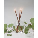 Everlasting Candles Copper, Candles Only, Set of 3 with lit copper-colored candles arranged in a clear round vase, styled with green eucalyptus leaves, perfect for home decor and gifts. 1