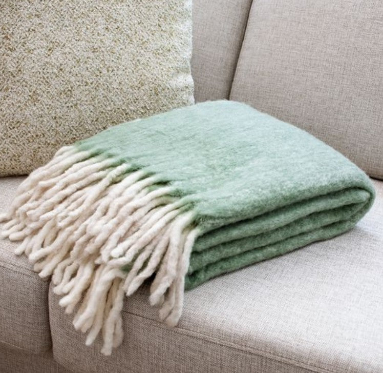 Soft green and cream wool blend throw with fringe detailing folded on a beige sofa, ideal decor and gift from Knotty and Board, every room needs a little Knotty and Board, Green Wool Blend Throw 50 x 60