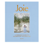 Joie book with a blue cover featuring a photo of a woman in a floral dress standing by a flower-covered stone wall, celebrating Parisian lifestyle and decor themes. 1