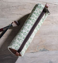Green Floral Canvas Pencil Case 8.5" with a leafy pattern and brown zipper, displayed on a wooden surface alongside two makeup brushes, enhancing decor and gifting options.