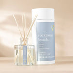 Rockaway Beach Reed Diffuser with clear glass bottle, natural reeds, and light blue labeled packaging, perfect for adding fresh decor and fragrance to any room. 1