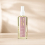 Rockaway French Citrus Room Spray in a clear spray bottle with a white nozzle, featuring a pink label, placed on a light wood surface with soft natural light and shadows in the background. 1