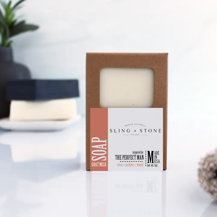 A packaged bar of Men's Soap, Perfect Man, Citrus Jasmine Woods, 5 oz., in a brown box with a white and orange label, displayed on a clean, modern surface with minimal decor in the background, ideal for gifts and stylish home decor from Knotty and Board.