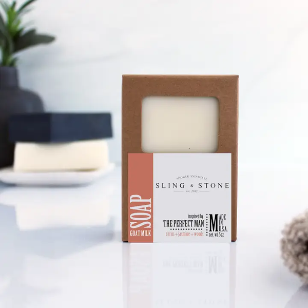 A packaged bar of Men's Soap, Perfect Man, Citrus Jasmine Woods, 5 oz., in a brown box with a white and orange label, displayed on a clean, modern surface with minimal decor in the background, ideal for gifts and stylish home decor from Knotty and Board.