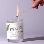 Hand lighting a Just Bee Sandalwood Fern Candle, 7 oz. with a long match, showcasing a minimalist glass candle with fern decor and natural scent, perfect for home gifts and decor. 1