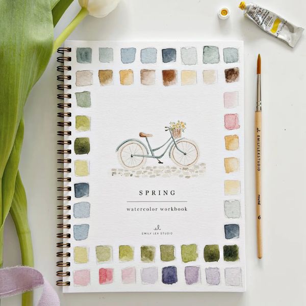 Watercolor Workbook, Spring featuring a spiral-bound cover with a painted bicycle and floral basket surrounded by colorful swatches, a paintbrush, and a tube of watercolor paint next to a tulip leaf on a white surface, offered by Knotty and Board with the tagline Every Room Needs A Little Knotty and Board.