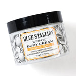 Jar of Blue Stallion Whipped Body Cream, Orange Tango with black lid and decorative citrus fruit and leaf design, a curated gift from Knotty and Board for decor and personal care. 1