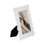Decorative Scallop Edge Resin Photo Frame, White, 4 X 6 in. standing on black easel back, showcasing a modern minimalist art print with greenery, perfect for home decor or gifts from Knotty and Board. 1