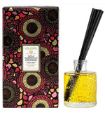 Voluspa Goji Tarocco Orange Reed Diffuser 3.4 oz with black reeds in a textured glass bottle filled with yellow liquid, next to a colorful floral patterned box, perfect for kitchen or dining decor from Knotty and Board, Every Room Needs A Little Knotty and Board. 1