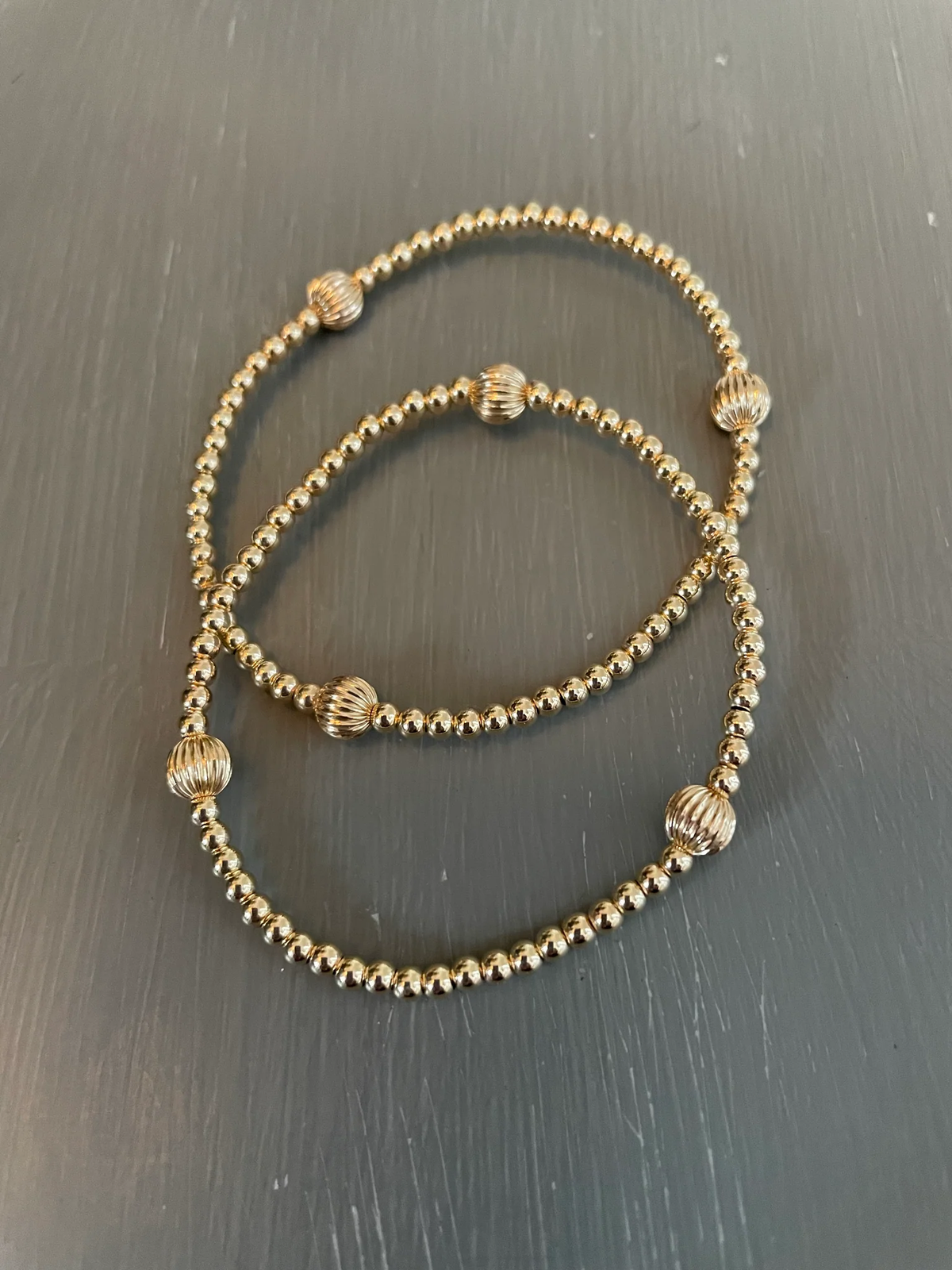Morgan & Me 4mm 14k Gold Filled Bracelet with 14k Gold or Sterling Silver Bead displayed on a dark surface, showcasing delicate gold beads with textured accent beads, a perfect jewelry gift from Knotty and Board.