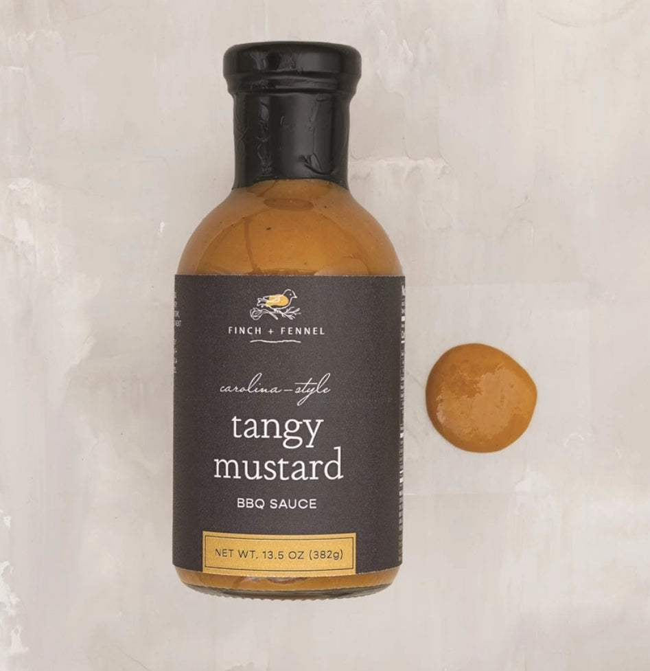 Bottle of Finch & Fennel Carolina-Style Tangy Mustard BBQ Sauce, 13.5 oz with a small dollop of sauce on a light surface, perfect for kitchen and entertaining gifts at Knotty and Board.