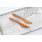 Two handcrafted Fruitwood Butter Spreader, Set of 2 resting on a white marble surface, ideal for kitchen decor and entertaining with a warm natural wood finish. 2