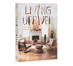 Book cover of Living Upriver featuring a cozy living room with wooden furniture and a burning fireplace, showcasing charming home decor and rustic style. 1