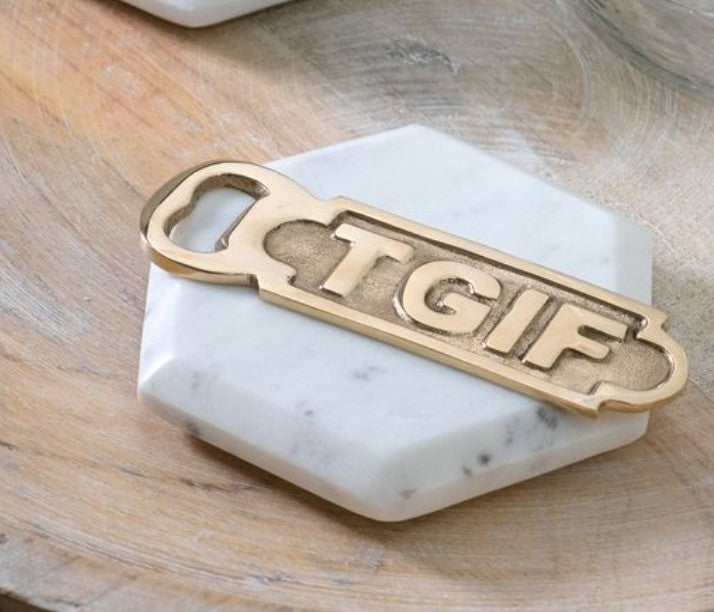 Brass TGIF Bottle Opener resting on a white marble hexagonal coaster on a wooden surface, perfect for kitchen or entertaining decor.