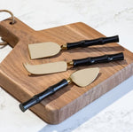 Black Gold Cheese Knife Set with sleek gold blades and black bamboo-style handles displayed on a wooden cutting board, perfect for kitchen decor and entertaining gifts by Knotty and Board. 2