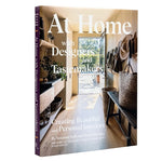 At Home with Designers book cover showing a warm, inviting entryway with natural light, decor accents, woven baskets, and hanging hats, embodying thoughtful interior design style. 1