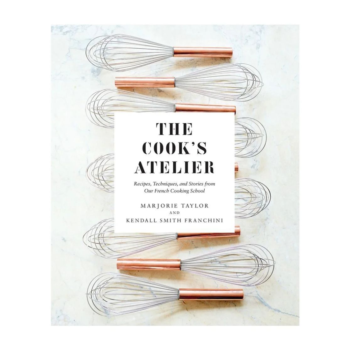 Cook's Atelier Book pictured with copper-handled whisks on a marble surface, highlighting kitchen decor and culinary inspiration from Knotty and Board, an independent brick and mortar retail.