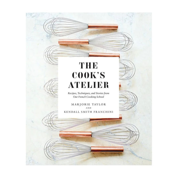 Cook's Atelier Book pictured with copper-handled whisks on a marble surface, highlighting kitchen decor and culinary inspiration from Knotty and Board, an independent brick and mortar retail.
